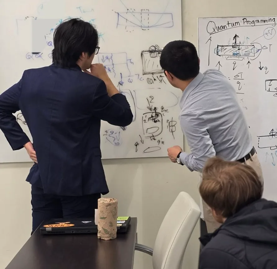 Two people work through quantum programming sketches on a whiteboard while a third looks on